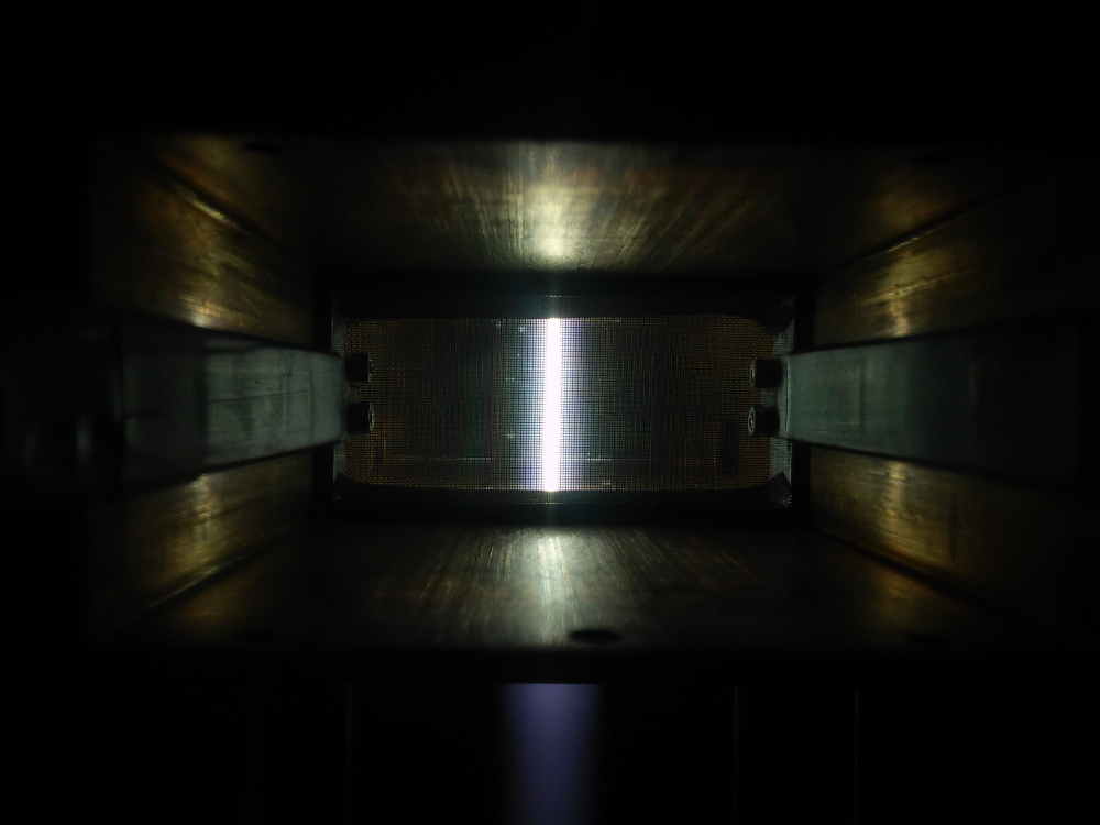 Een kijkje in het hart van de plasmareactor. Achter een metalen gaas dat de magnetronstraling tegenhoudt licht de buis met plasma op